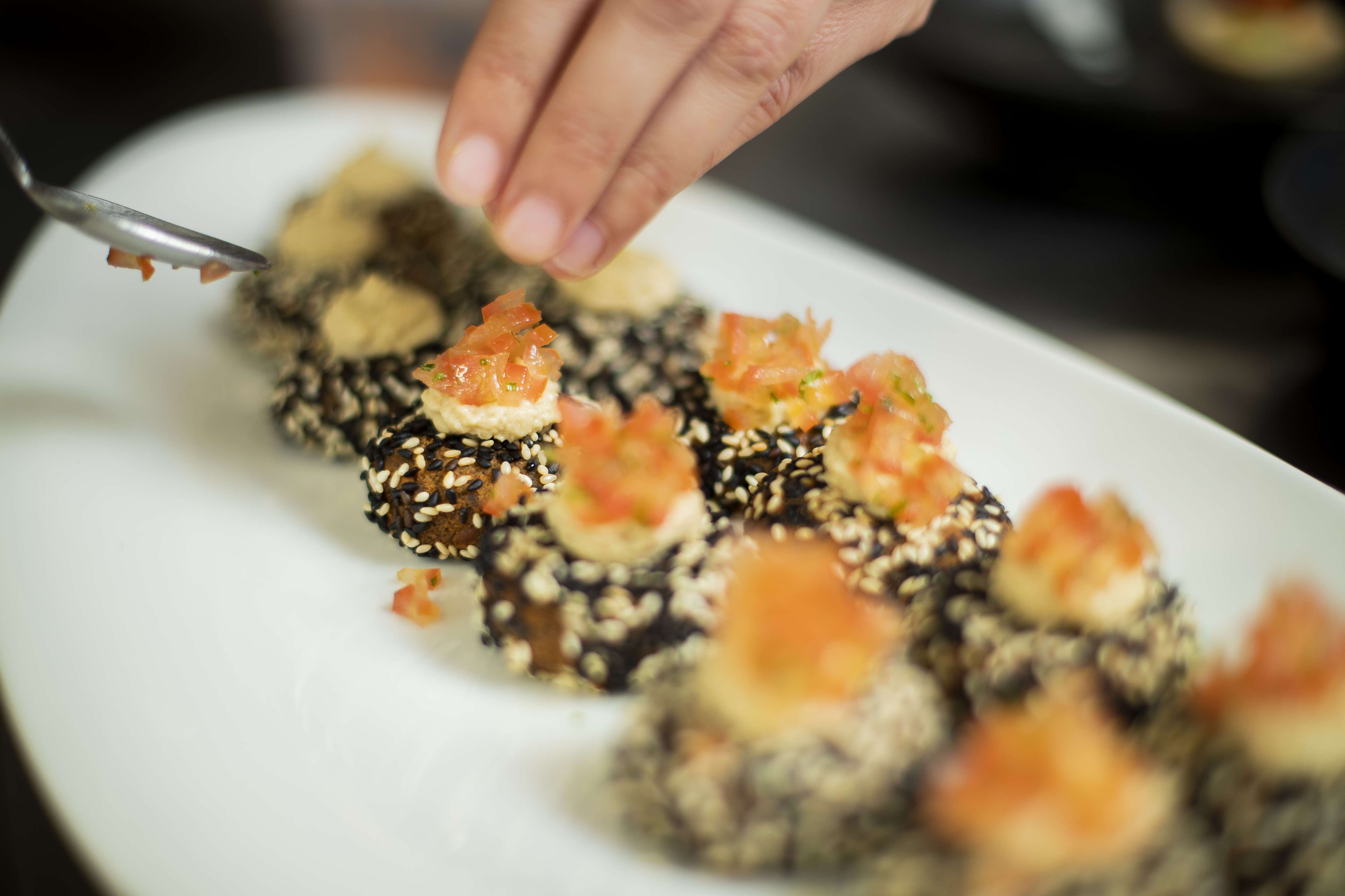Close up of plchef garnishing a platter of Felafel with hummus and tomato salsa. Photo: Richard Jupe.