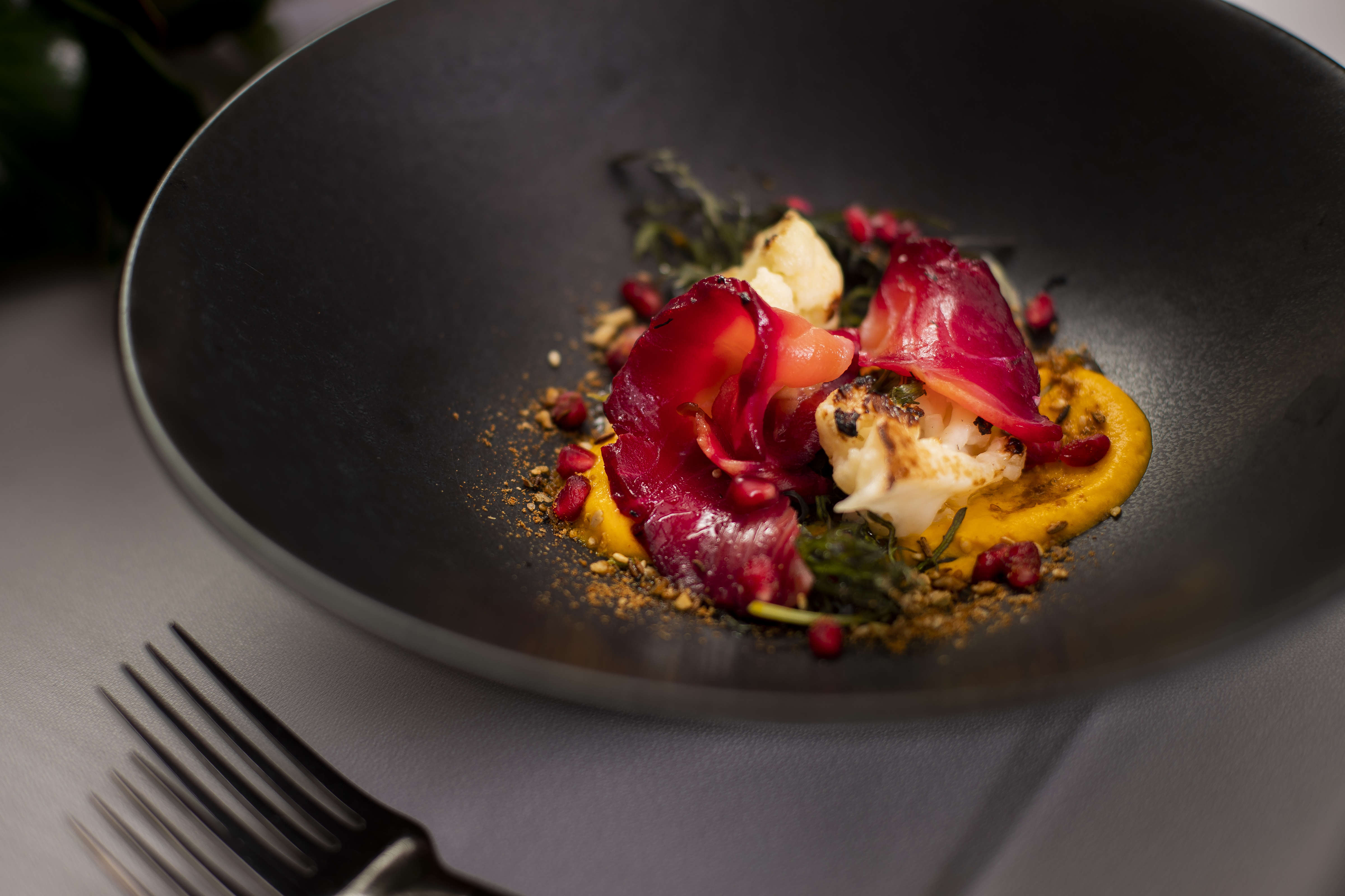 Close up photo of a black bowl with beetroot cured salmon, cauliflower, carrot puree, pomegranate seeds and dukkah. Photo: Richard Jupe.